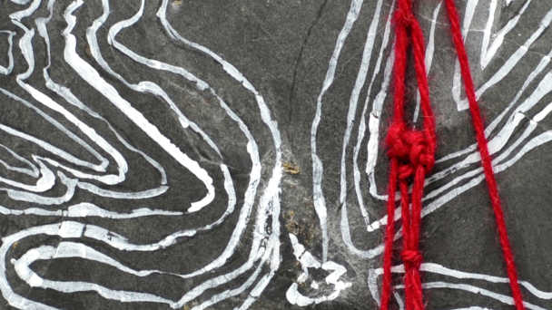 Détail motif ethnique blanc peint sur une ardoise et fil de laine rouge par Sylvie Hénot
